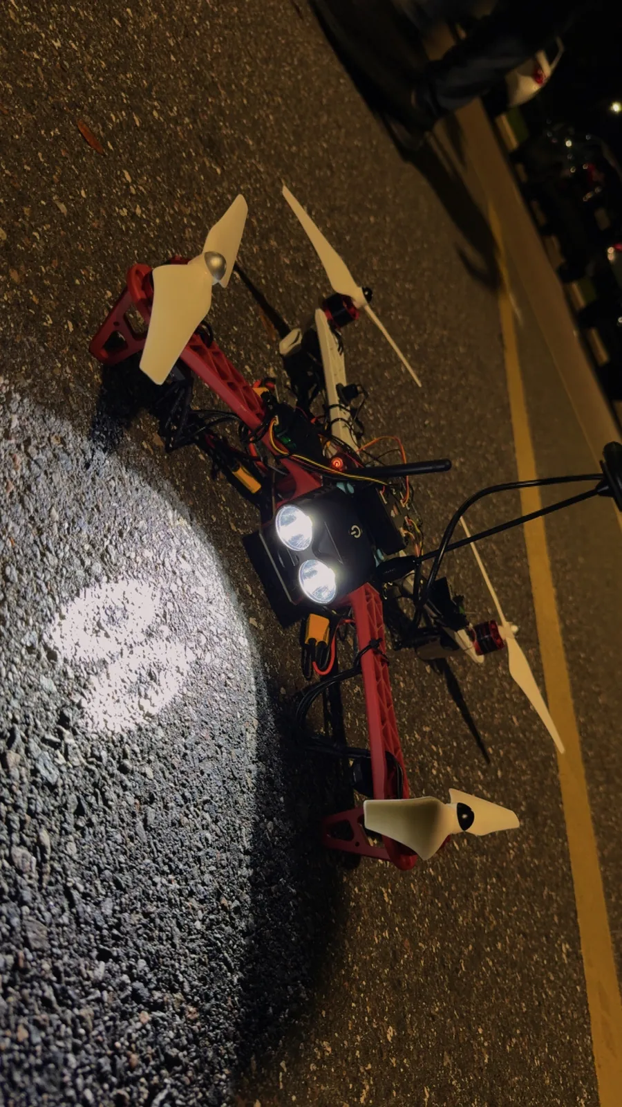The F450 quadcopter on asphalt at night, its twin LED lights on
